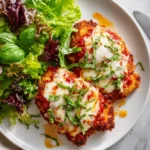 A golden-brown Chicken Parmigiana topped with melted cheese and fresh basil, served with pasta, showcasing classic Italian comfort food.